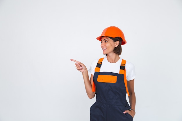 Uma engenheira bonita na construção de um capacete protetor em um sorriso confiante e branco apontando o dedo esquerdo