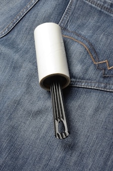 Uma escova para roupas pegajosa enrolada em rolos repousa sobre jeans escuros.