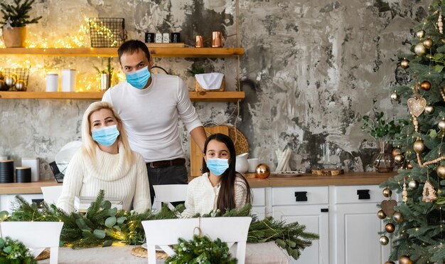 Uma família feliz usa máscaras médicas devido ao coronavírus COVID-19 perto da árvore de Natal. feriados de natal.