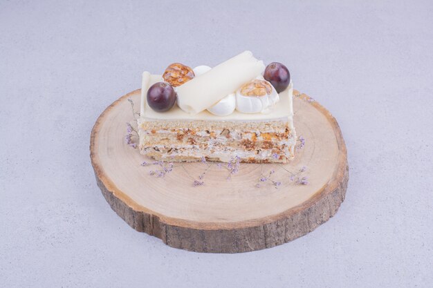 Uma fatia de bolo com nozes e uvas na placa de madeira.