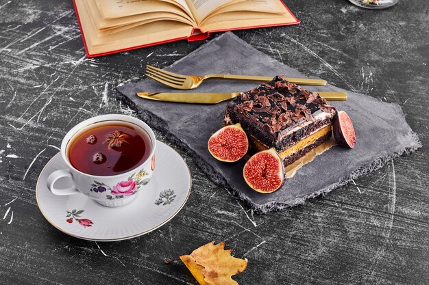 Uma fatia de bolo de chocolate com figos e chá numa travessa de pedra.