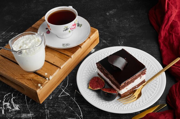 Uma fatia de bolo de chocolate com frutas e uma xícara de chá e requeijão.