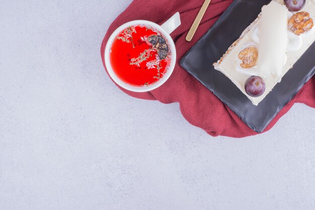 Uma fatia de bolo em uma travessa de cerâmica com uma xícara de chá vermelho de ervas.