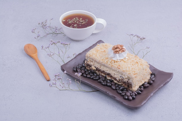 Uma fatia de bolo medovic com grãos de chocolate em uma travessa preta com uma xícara de chá