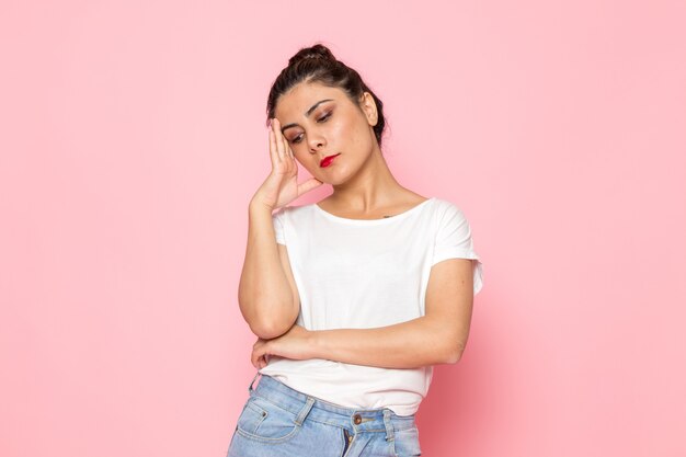 Uma fêmea jovem de vista frontal em camiseta branca e calça jeans azul posando com expressão de pensamento