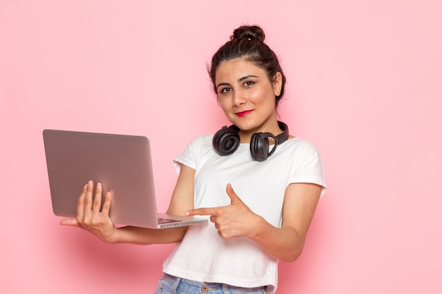 Foto grátis uma fêmea jovem vista frontal em camiseta branca e calça jeans azul usando laptop com fones de ouvido