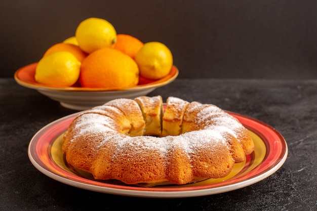 Uma frente fechou a vista doce redondo bolo com açúcar em pó fatiado doce delicioso bolo isolado dentro da placa junto com limões e fundo cinza biscoito de açúcar