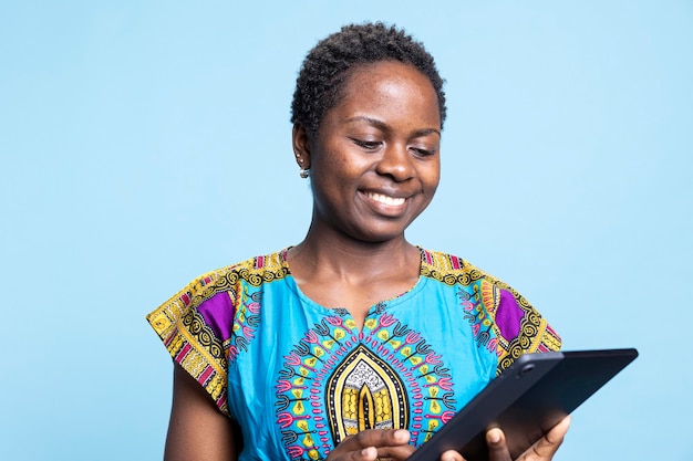 Uma garota afro-americana está feliz em usar um tablet contra um fundo azul.