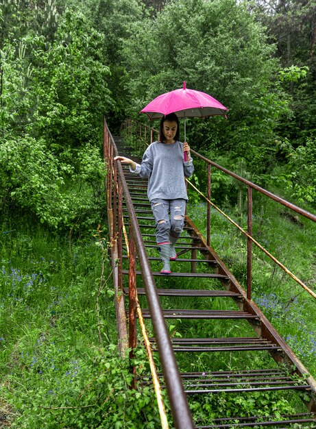 Uma garota com um guarda-chuva caminha na floresta em um clima chuvoso