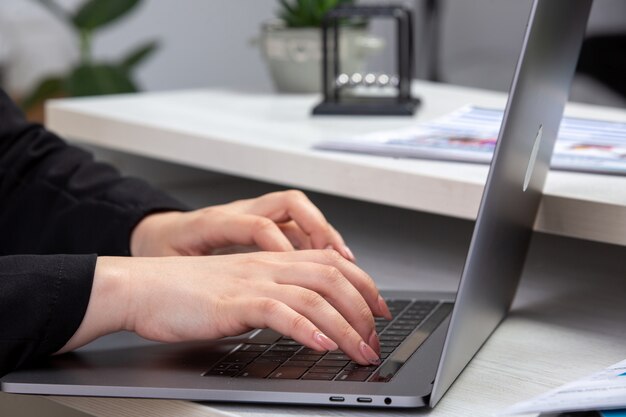 Uma garota de vista frontal usando o laptop na frente da mesa com agendas e gráficos e usando a atividade comercial de trabalho de laptop