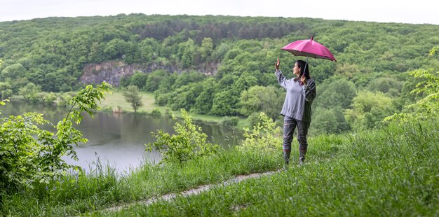 Uma garota em uma caminhada na floresta sob um guarda-chuva entre as montanhas perto do lago.