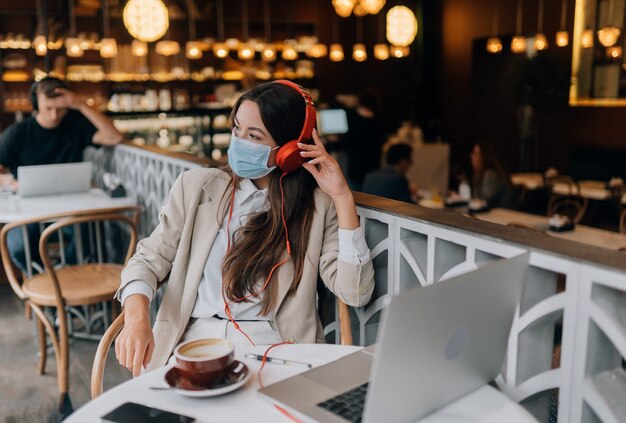 Uma garota sentada em uma cafeteria com surto de coronavírus em fones de ouvido