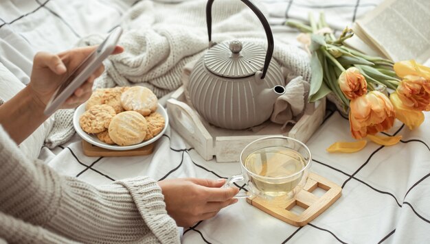 Uma garota tira fotos ao telefone de uma composição de primavera com chá, biscoitos e tulipas na cama