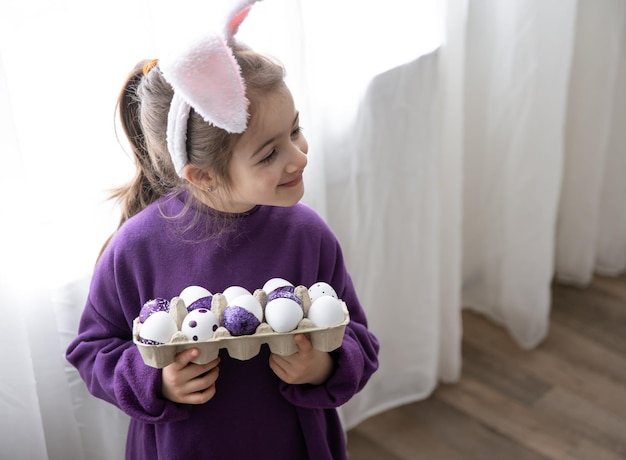 Uma garotinha com orelhas de páscoa segura uma bandeja de ovos de férias
