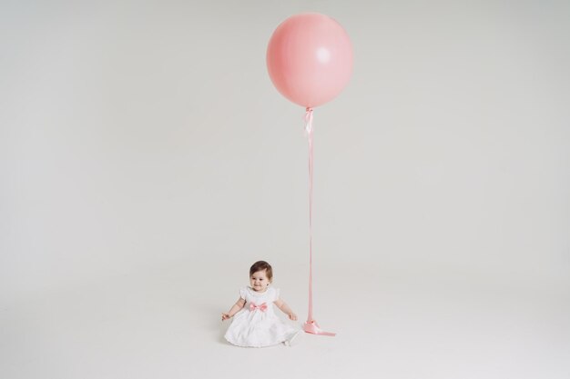 Uma garotinha com um grande balão rosa de vestido branco em um fundo branco