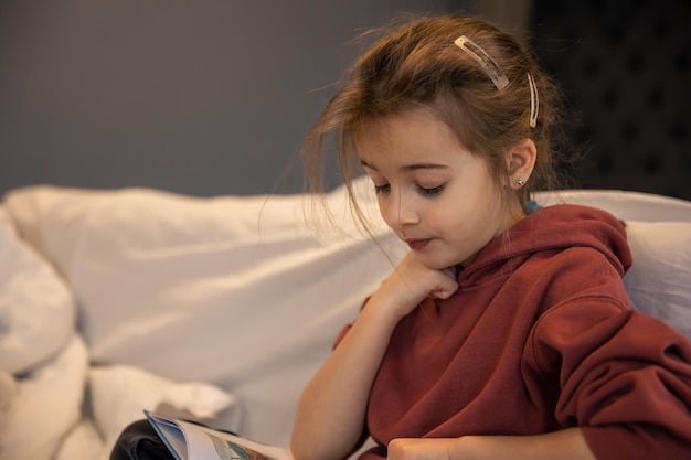 Uma garotinha está lendo um livro enquanto está sentada em seu quarto