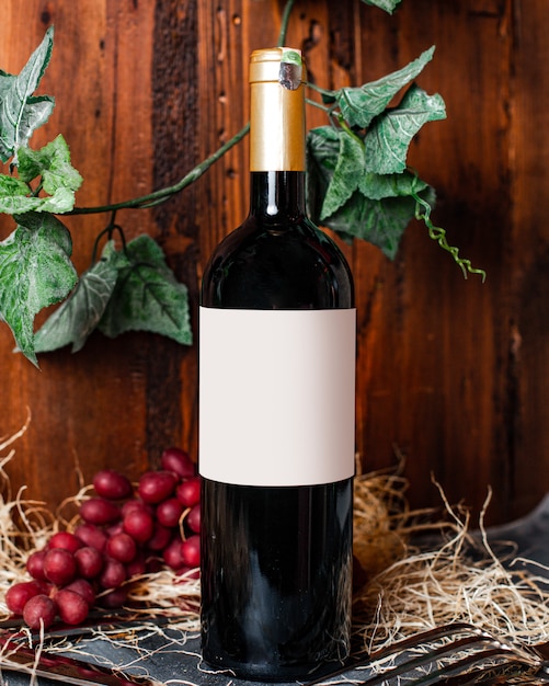 Uma garrafa de vista frontal de vinho vinho tinto com tampa dourada, juntamente com bagas e folhas verdes na adega de álcool de fundo