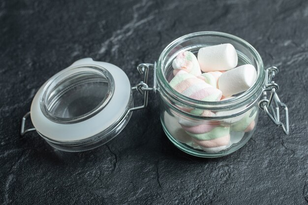 Uma jarra de vidro cheia de marshmallows em uma superfície escura.