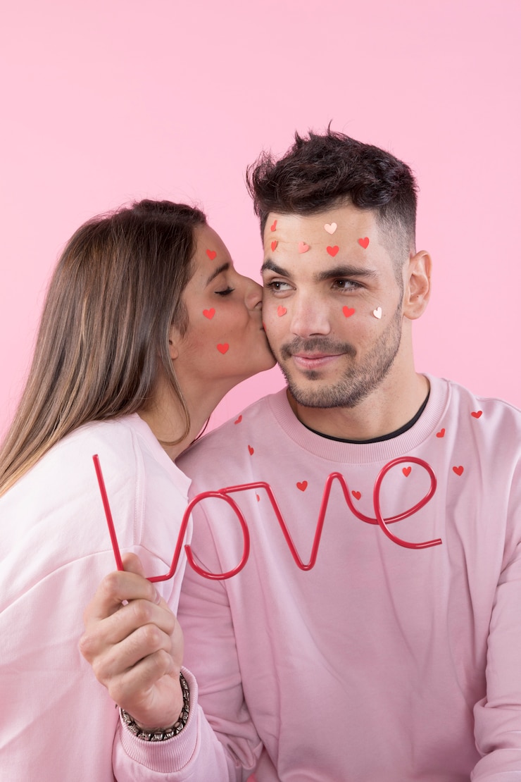 Foto grátis uma jovem a beijar um tipo com corações de papel no rosto e um sinal de amor.