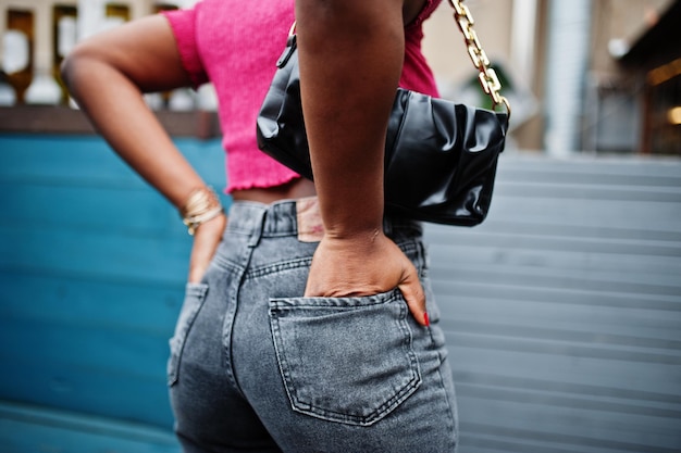 Uma jovem afro-americana urbana em top rosa e jeans cinza com bolsa Afro fashion chic mulheres nas costas