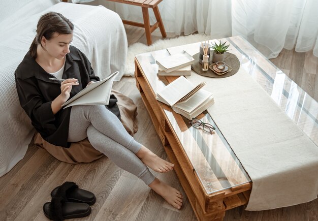 Uma jovem aluna faz tarefas em casa, sentada com um caderno nas mãos.