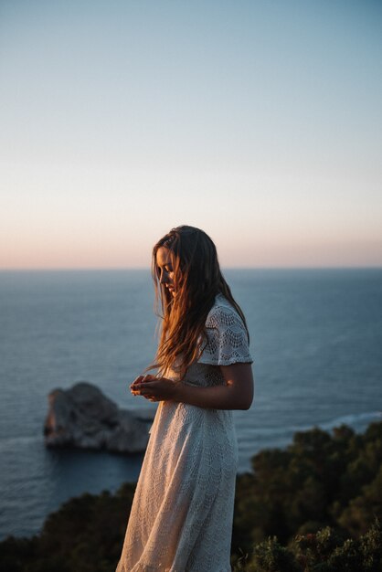 Uma jovem atraente com um lindo vestido branco caminhando à beira-mar à noite