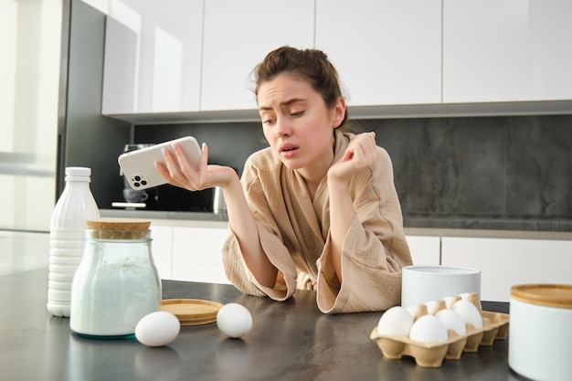 Foto grátis uma jovem atraente e alegre assando na cozinha fazendo massa segurando um livro de receitas com ideias