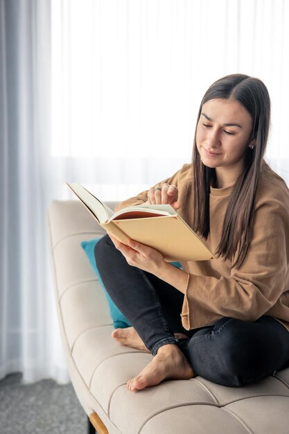 Uma jovem atraente está lendo um livro enquanto está sentada no sofá