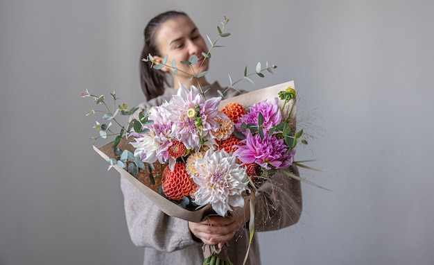 Uma jovem atraente sorri e segura um grande buquê festivo com crisântemos e outras flores nas mãos. Foto Premium