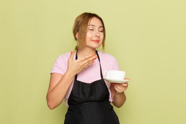 Uma jovem cabeleireira feminina de camiseta rosa e capa preta segurando o copo sorrindo no verde