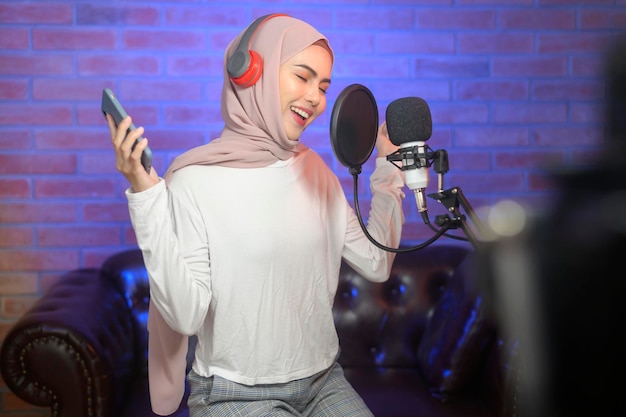 Uma jovem cantora muçulmana sorridente usando fones de ouvido com microfone enquanto gravava música