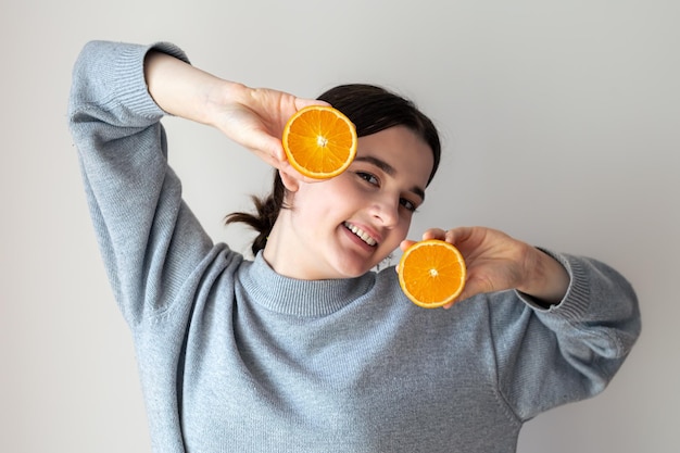 Uma jovem com metades apetitosas de uma laranja em um fundo branco