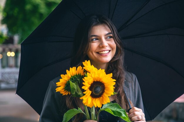 Uma jovem com um buquê de girassóis sob um guarda-chuva em tempo chuvoso