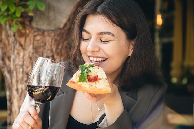 Uma jovem com um copo de vinho e uma fatia de pizza em um restaurante