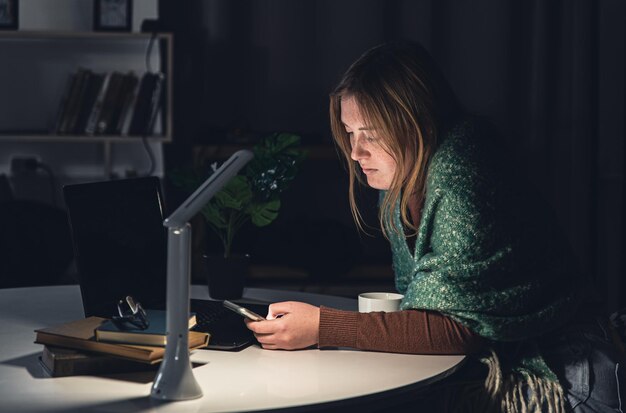 Uma jovem com um smartphone nas mãos trabalha tarde da noite