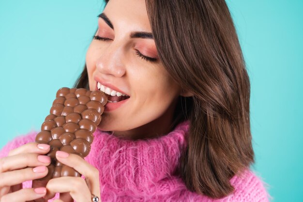 Foto grátis uma jovem com um suéter multicolorido brilhante em azul aprecia cada pedaço de uma deliciosa barra de chocolate ao leite arejado