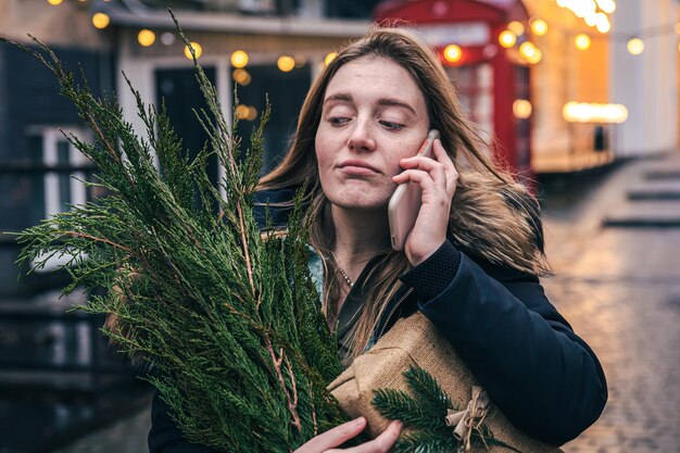 Uma jovem com uma árvore de natal e uma caixa de presente falando ao telefone