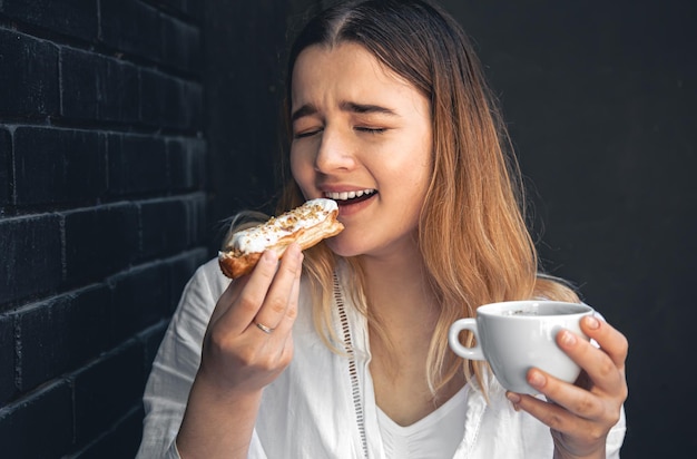 Foto grátis uma jovem com uma xícara de café e um eclair nas mãos