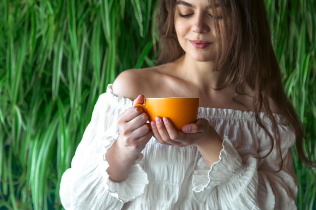 Foto grátis uma jovem com uma xícara de café no fundo com plantas verdes