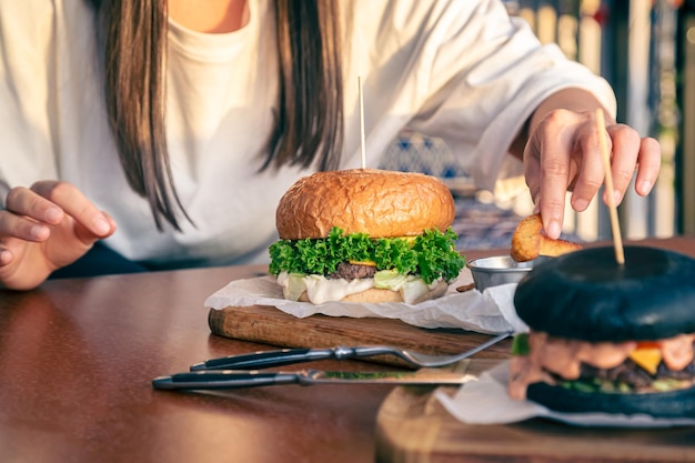 Foto grátis uma jovem comendo hambúrguer em um café de rua de perto