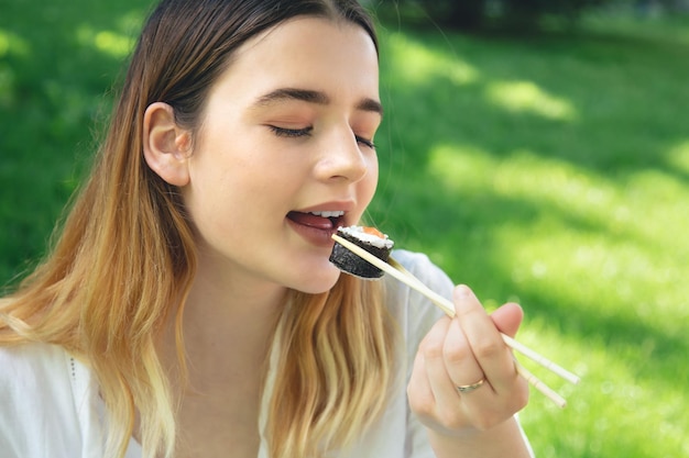 Uma jovem comendo sushi na natureza maki roll closeup