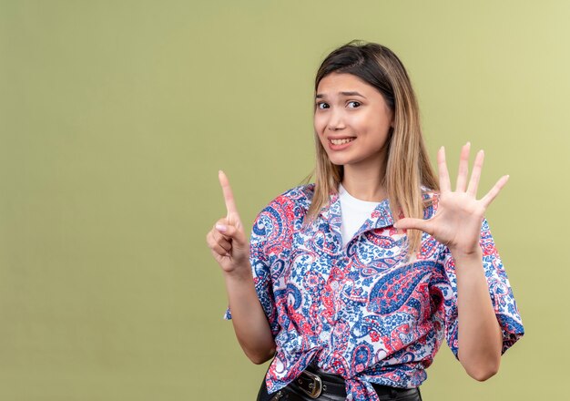 Uma jovem confusa vestindo uma camisa estampada de paisley mostrando o número seis