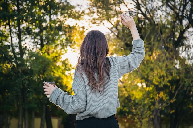 Uma jovem de suéter com uma xícara de café na natureza