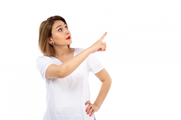 Uma jovem de vista frontal em camiseta branca posando apontando para o céu em branco
