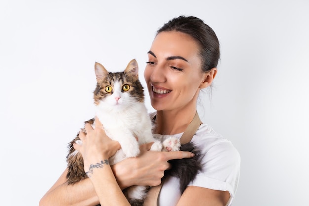 Uma jovem dona de casa de avental sobre fundo branco segura seu amado animal de estimação, um grande gato fofo, uma família feliz