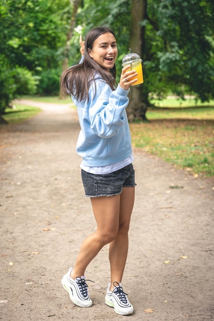 Uma jovem em uma caminhada no parque com suco de laranja