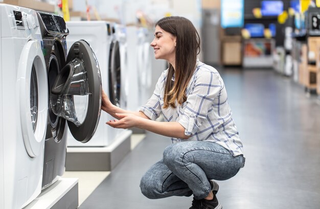Uma jovem em uma loja escolhe uma máquina de lavar.