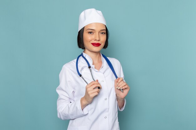 Uma jovem enfermeira de vista frontal em um terno médico branco e um estetoscópio azul sorrindo na mesa azul.