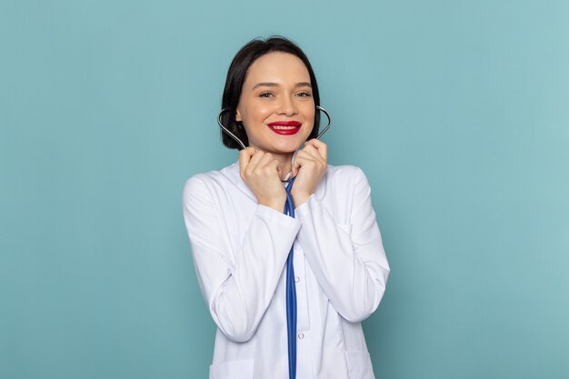 Uma jovem enfermeira de vista frontal em um terno médico branco e um estetoscópio azul sorrindo na mesa azul.