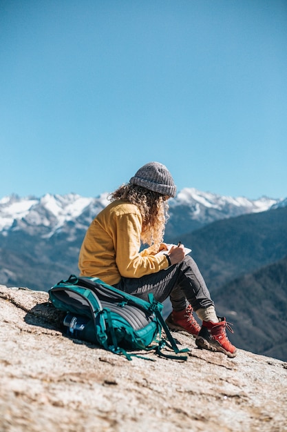 Uma jovem escrevendo em seu livro enquanto está sentada em uma colina perto de uma montanha
